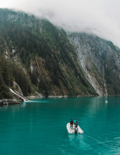 Tender with three people cruising towards a small waterfall in Alaska