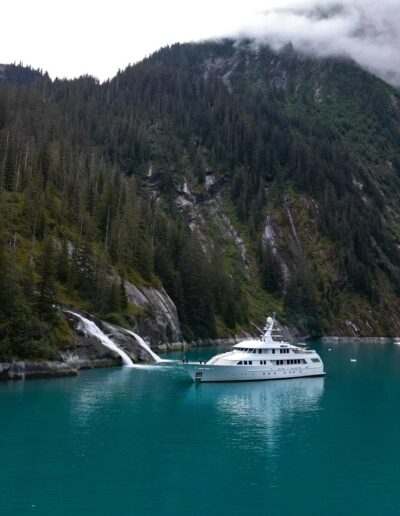 Drone footage of a yacht cruising by a waterfall. Dramatic cliffs in the background.