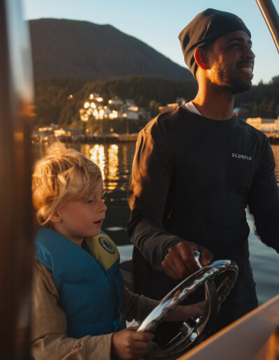 Closeup of a young man and child steering a boat during sunset in Alaska.