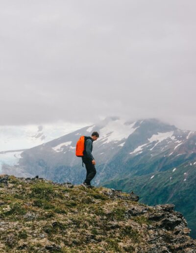 A young man hiking in Alaska, surrounded by snow covered mountains.